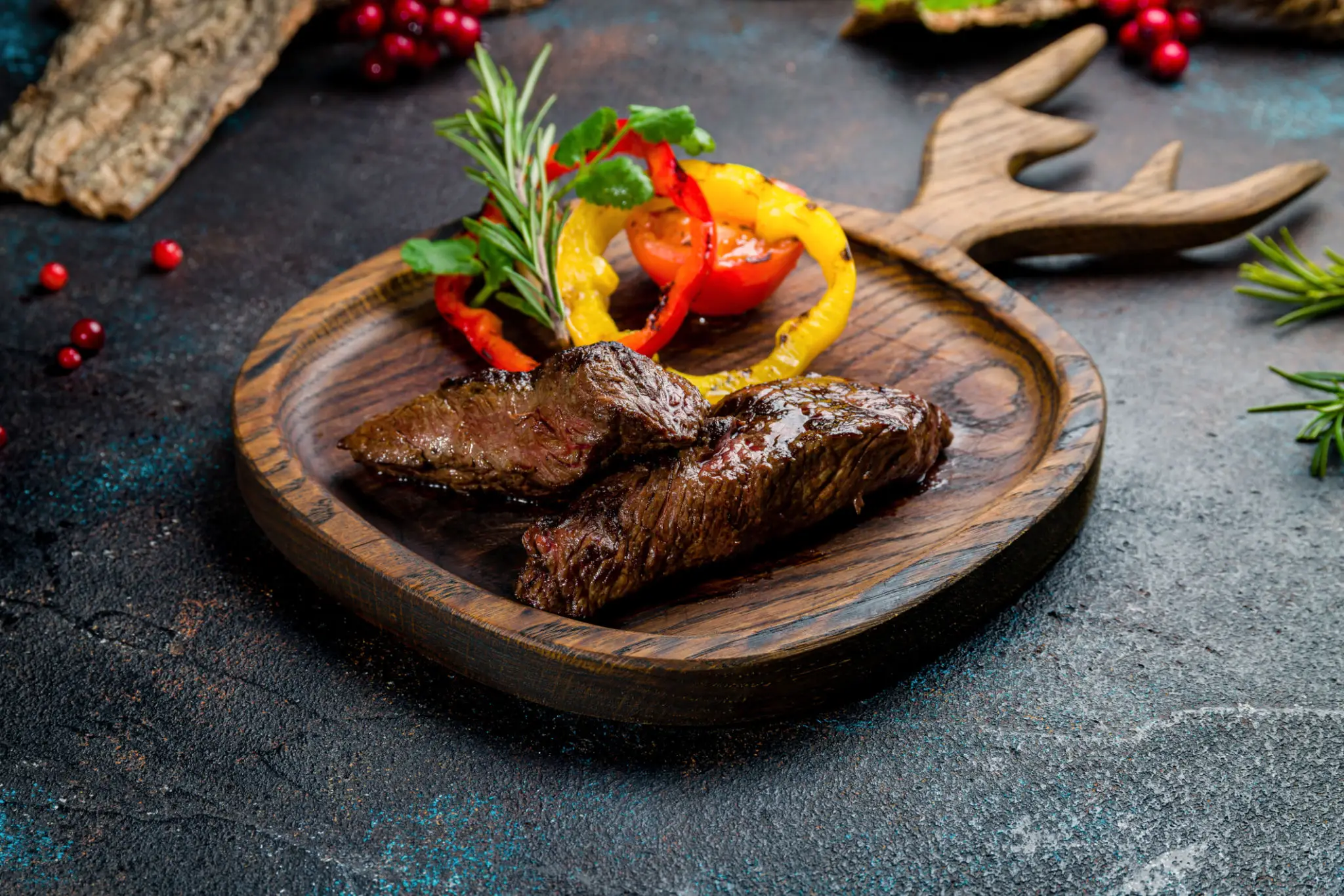 Grilled steak served with colorful roasted vegetables on a wooden plate.