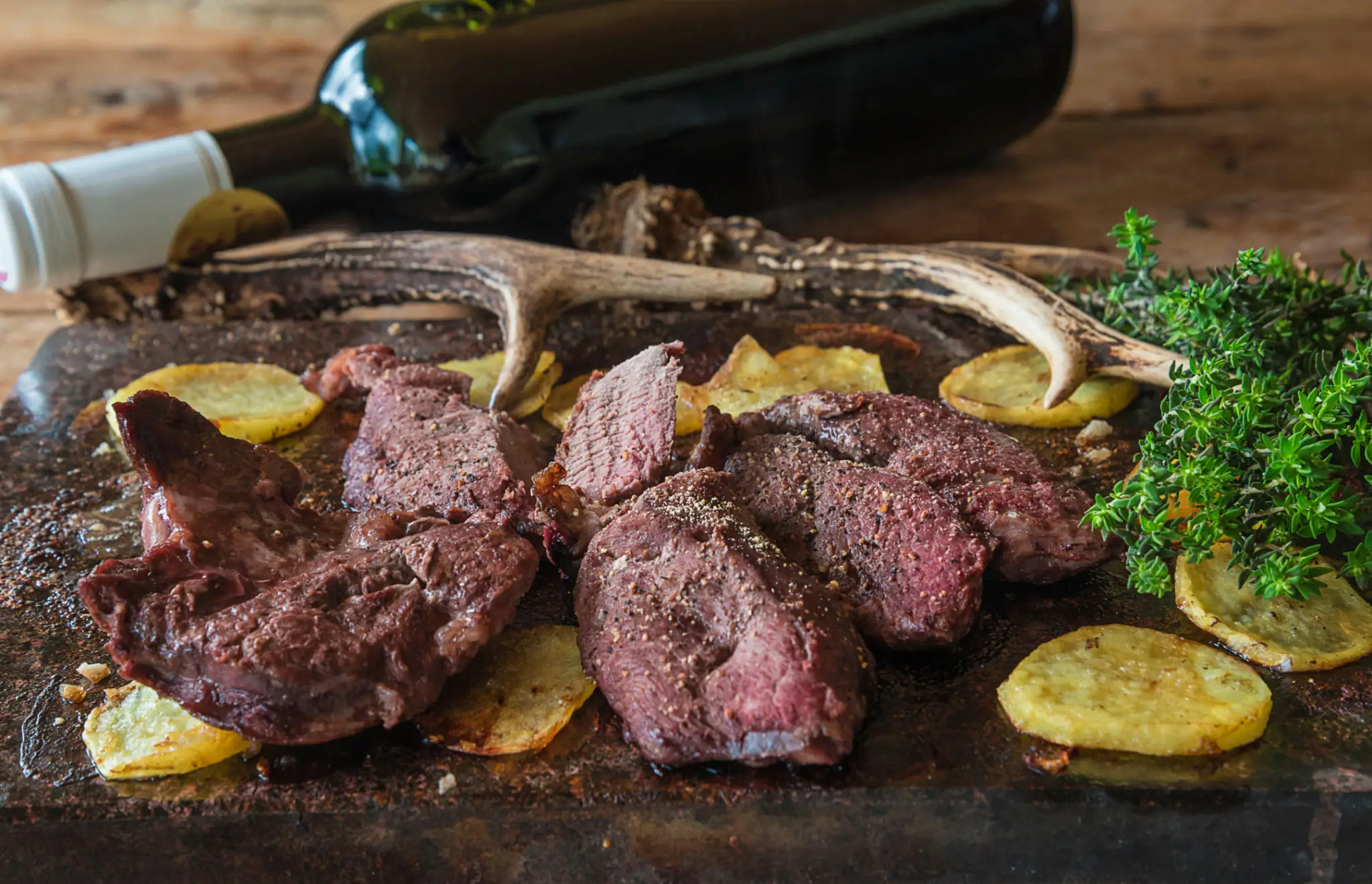Close-up of cooked steak slices with potatoes and herbs on a wooden board.