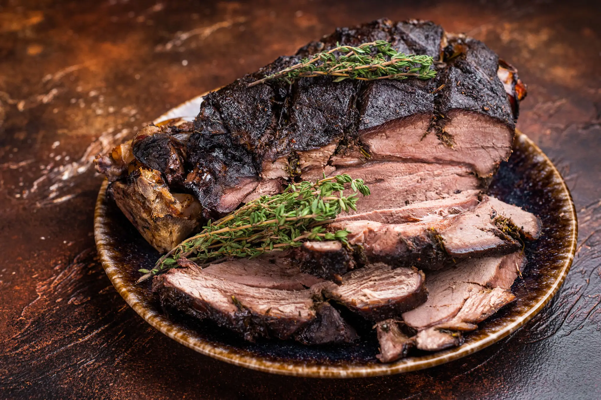 Sliced roasted beef garnished with herbs on a wooden plate.