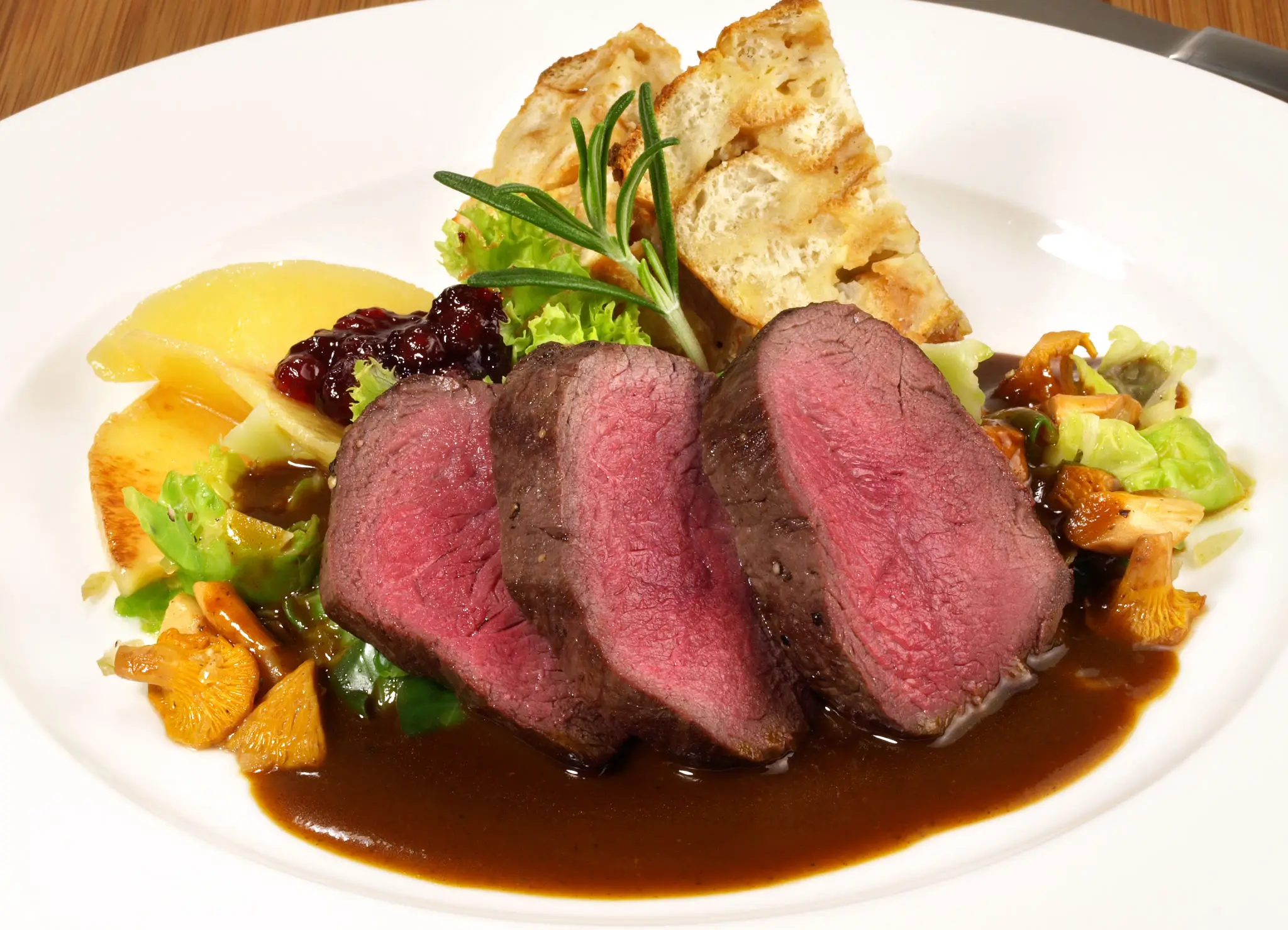 Three slices of medium-rare steak with sauce and sides.