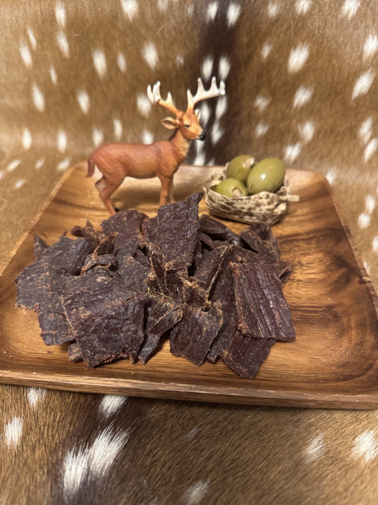 Sliced beef jerky on a wooden plate with a decorative deer and eggs.